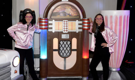 Women standing by giant jukebox prop at American diner themed party